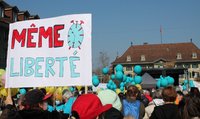  Un rassemblement de personnes. Au premier plan, une pancarte "Même Liberté" est brandie.