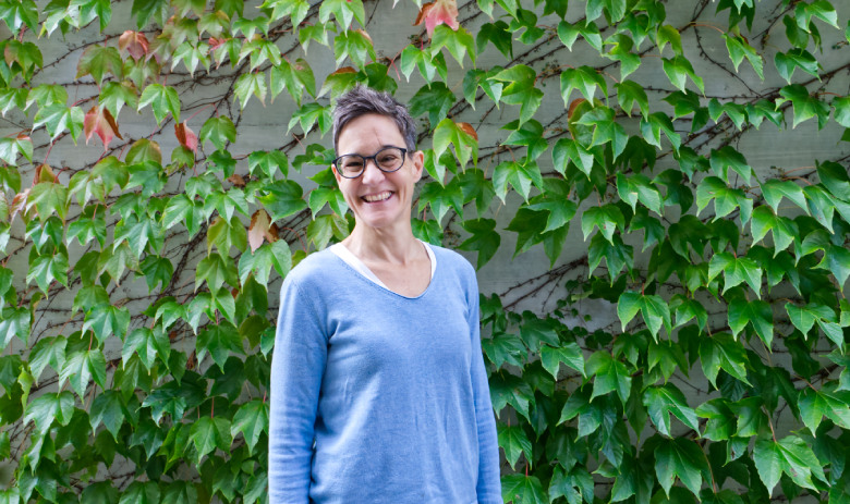 Julia Eugster Julia Eugster blickt lächelnd in die Kamera und steht vor einem grünen Hintergrund mit vielen Pflanzen.