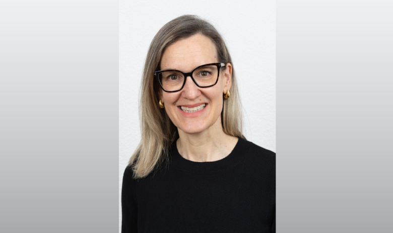 Portraitfoto einer Frau mit blonden Haaren und Brille. Sie trägt einen schwarzen Pullover und lächelt in die Kamera.